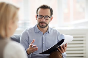 Male counselor in a blue shirt and glasses, with pen and document explaining something